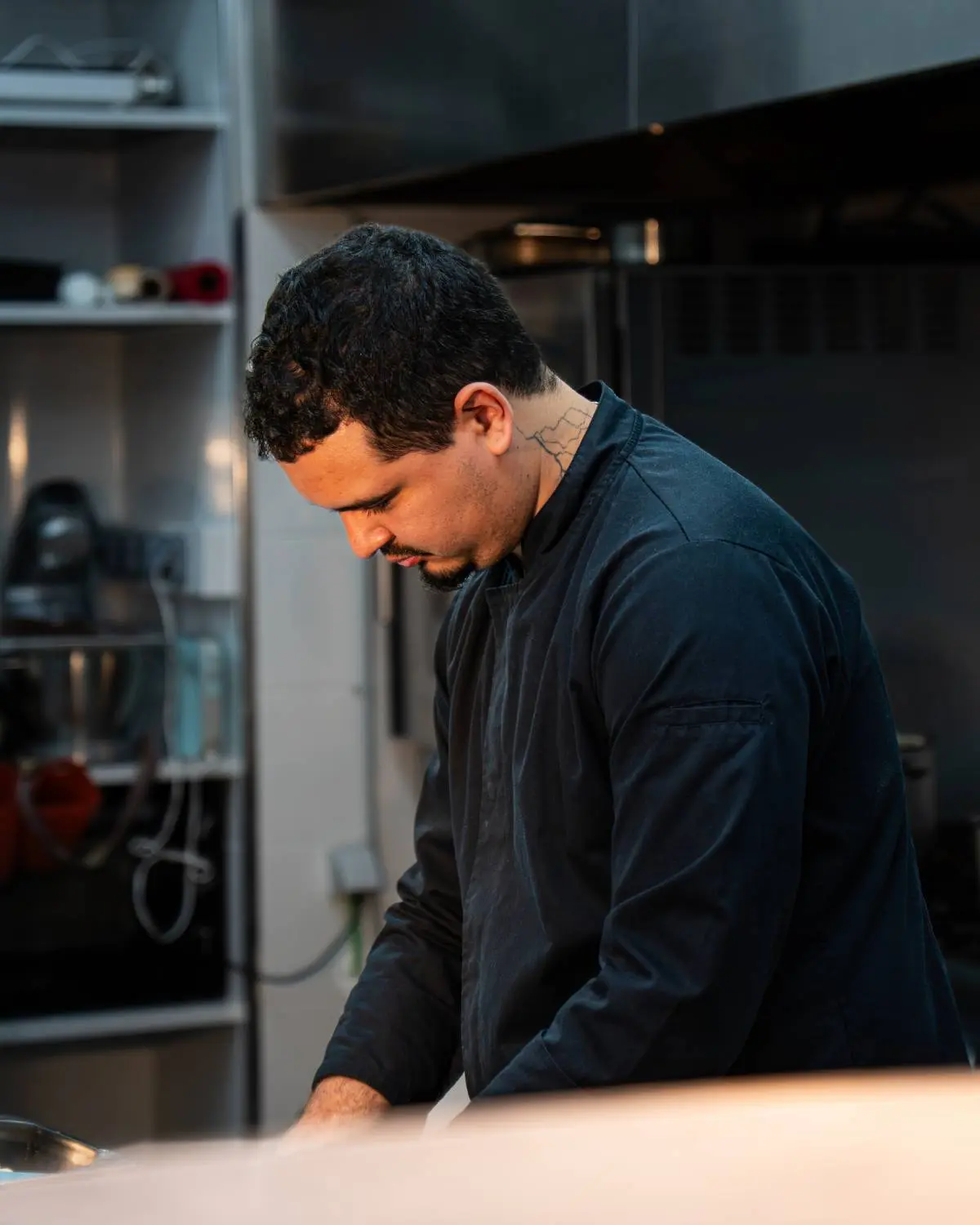 O Chef Sarano de jaleca preta, concentrado numa cozinha profissional.